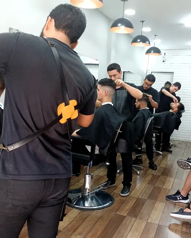 Salão da Homem Atual com cinco barbeiros atendendo ao mesmo tempo, luminárias pendentes e piso de madeira
